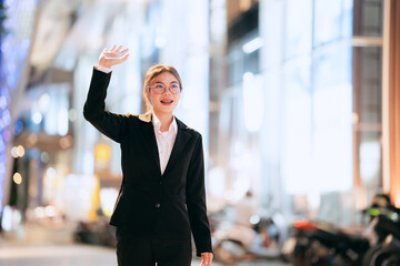 Confident young businesswoman in a black suit standing outdoors at night, smiling with arms...