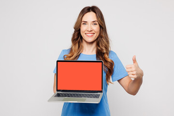 Young IT woman wears blue t-shirt casual clothes hold use work on laptop pc computer with blank screen workspace area show thumb up isolated on plain solid white color background. Lifestyle concept.