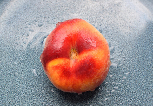 Red ripe flat peach on blue plate. One fig peach in water drops. Fresh tasty peach