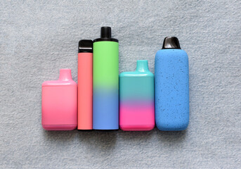 Several multi-colored electronic cigarettes lie on denim. Vape with nicotine.