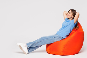 Full body young calm woman wears blue t-shirt casual clothes sit in bag chair hold hands behind her...