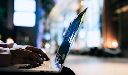 Close-up of a person typing on a laptop at night with blurred lights in the background, symbolizing...