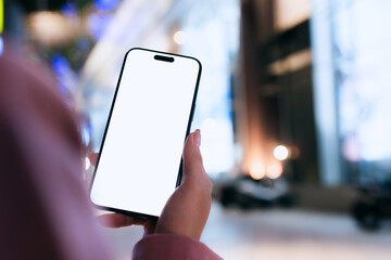 A close-up of a woman using a smartphone with a blank white screen at night. Technology, communication, and digital interaction in a modern urban setting.