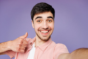 Close up young man he wears pink shirt t-shirt casual clothes doing selfie shot pov on mobile cell phone thumb up isolated on plain pastel light purple background studio portrait. Lifestyle concept.