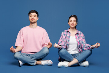 Full body young couple two friends family man woman they wear pink casual clothes together sit hold spread hands in yoga om aum gesture relax meditate try calm down isolated on plain blue background.