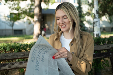 Beautiful and young blond woman portrait reading a newspaper in the park