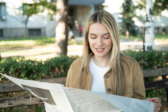 Beautiful and young blond woman portrait reading a newspaper in the park