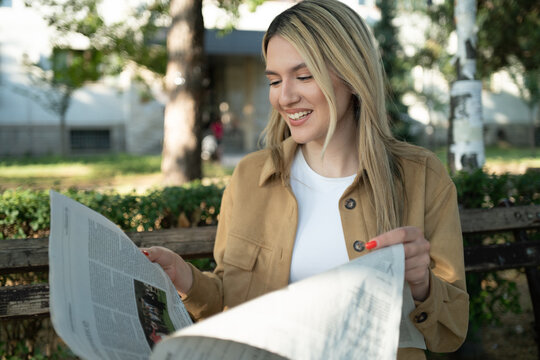 Beautiful and young blond woman portrait reading a newspaper in the park - Powered by Adobe