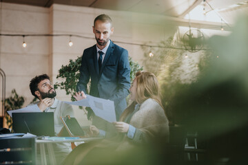 People discussing documents during a business meeting, seated in a stylish, plant-filled office....