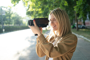 Happy female student videographer filming with an 8mm vintage camera on a sunny street on a summer day