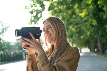 Happy female student videographer filming with an 8mm vintage camera on a sunny street on a summer...