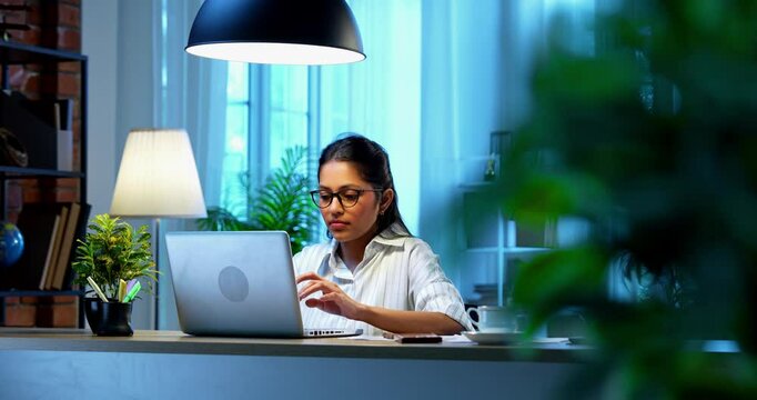 Indian businesswoman drafting email on laptop at desk in modern cozy office, Asian young female corporate executive typing an important message while thinking working remotely on wireless computer