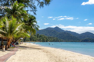Klong Prao Beach morning: crystal-clear turquoise sea with swimmers under palm trees, against mountainous island backdrop. Vibrant tropical paradise. Koh Chang, Thailand.

