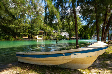 Small wooden dinghy on shore of Klong Prao's turquoise estuary channel, dappled sunlight filtering...