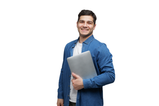 Young man smiles confidently holding a laptop while dressed casually in a denim jacket against a plain background