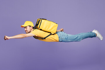 Full body young delivery guy employee man wear yellow cap t-shirt uniform workwear thermal bag work as dealer courier fly clench fist do super hero gesture isolated on plain pastel purple background.