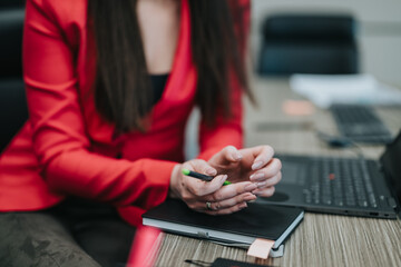 A focused businesswoman in a red blazer working with important documents and a laptop, sitting at a...