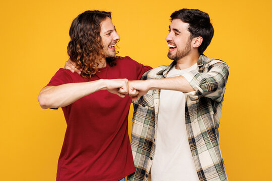 Young smiling happy two friends buddies men they wearing casual clothes together look camera do fist bump gesture isolated on plain yellow orange color background studio portrait. Lifestyle concept. - Powered by Adobe
