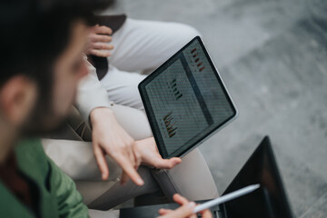 Two colleagues collaborate while reviewing business data visualized on a tablet, emphasizing...
