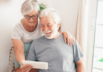 Video call concept. Bonding loving senior retired couple using digital tablet for online communication via video meeting, smiling white-haired man and woman looking and talking