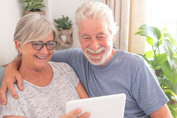 Video call concept. Bonding senior couple using digital tablet for online communication via video meeting, smiling white-haired man and woman enjoying tech and social