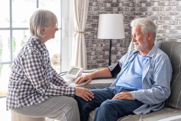 Senior woman using medical device to measure blood pressure of her husband suffering of...