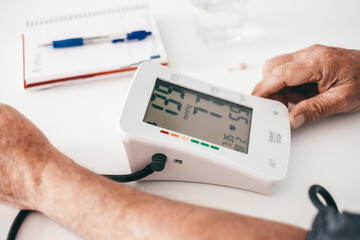 Old caucasian man using medical device to measure blood pressure - senior man suffering from...