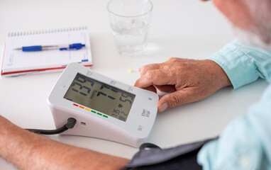 Old caucasian man using medical device to measure blood pressure - senior man suffering from...