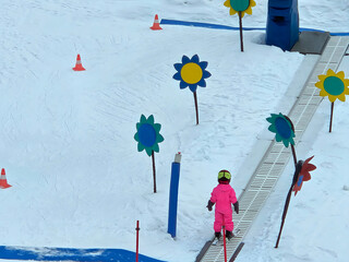 child are walking and training on a snow-covered slope with traveler. the child is wearing a pink...