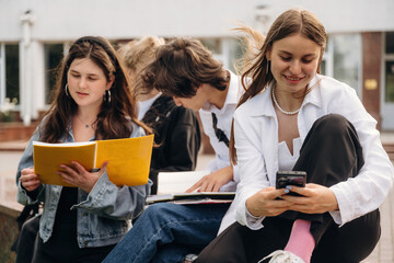 Learning, with phone and notepad or book. Group of students are near university together