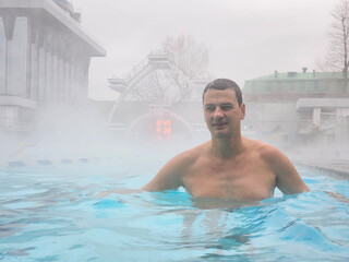 A man is in a pool of water, wearing only a shirt. The water is cold and misty, and the man is enjoying himself