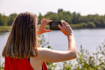 A woman capturing the beauty of a serene river landscape, with flourishing greenery perfectly...