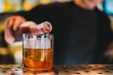 Close-up of a bartender pouring red liquor into a glass with ice cubes, set against a blurred bar...