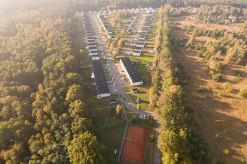 Aerial view of a modern residential development with white houses next to a forest at sunrise