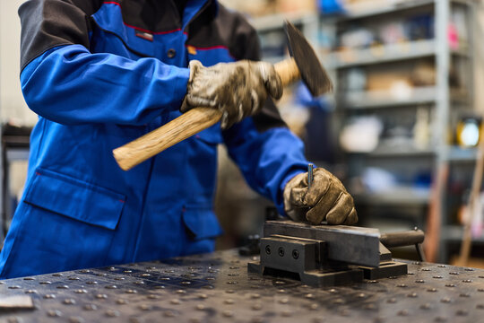 Worker in Blue Uniform Using Hammer on Metal Piece in a Workshop - Powered by Adobe