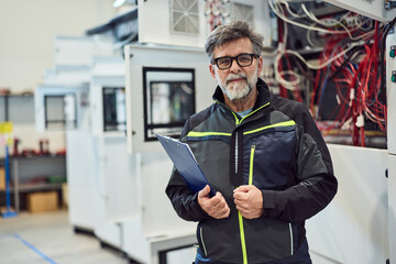 Engineer Standing Confidently in Factory Environment Holding Clipboard