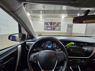 A black car is parked in a washing garage. The driver seat and wheel is in the middle of the car
