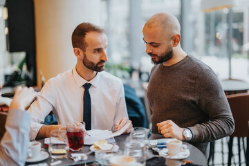 Male colleagues collaborate on a document at a cafe, displaying teamwork and professionalism in a...