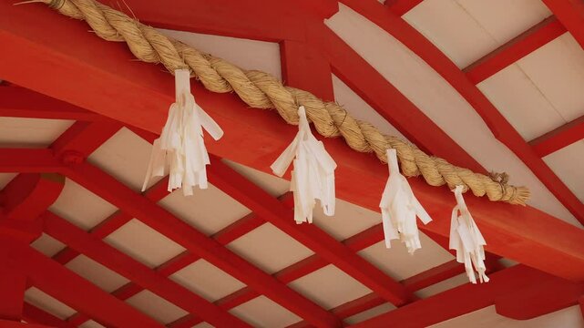 Traditional Japanese Shinto shrine shimenawa rope and paper shide under orange temple roof.