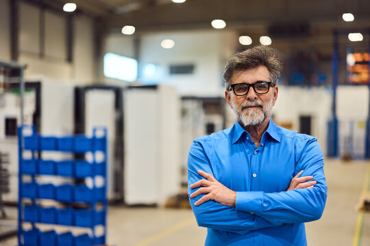 Confident Businessman Standing in Modern Industrial Warehouse with Arms Crossed