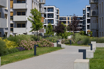 Modern residential buildings with landscaped courtyard, blooming flower beds, green trees and walking path on sunny day. Urban housing, outdoor space design and sustainable living
