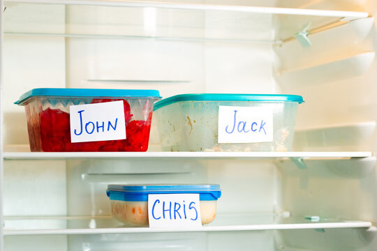 Meal containers labeled with employee names in clean office refrigerator. Lunch time for office workers.