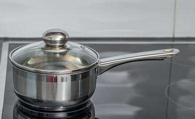 A stainless steel saucepan with a lid stands on an induction hob