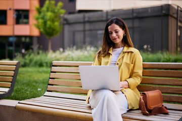 Woman Sitting on Park Bench Using Laptop in Urban Outdoor Setting