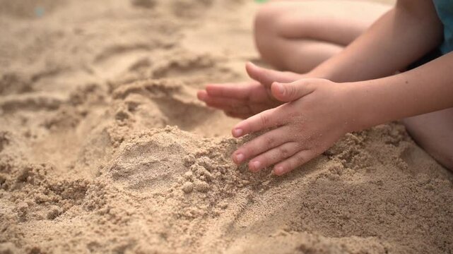 Hands of a child playing in a sandbox and building sand slides and castles.