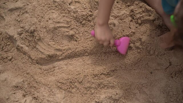 Child playing in sandbox with rake, building castles. Hands of a child playing in a sandbox and building sand slides and castles. Close-up video