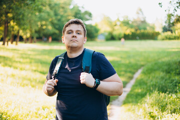 Sad 30s blonde man with backpack standing in the countryside. Traveler. Summer time. Portrait of young man in casual clothing standing outdoors