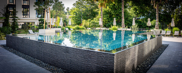 Contemporary Infinity Pool with Lush Garden Surroundings.  A beautifully designed infinity pool in a serene tropical environment, featuring sleek tile edges, poolside loungers, and parasols.