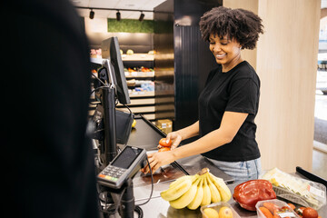 Smiling cashier weighing tomatoes at supermarket checkout
