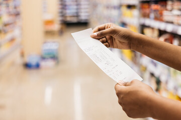 Customer checking grocery receipt in supermarket: inflation and budgeting concept